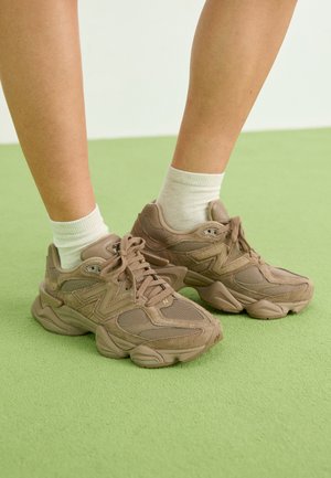 Ruske mokkasínit ja verkko sneakerit paksulla pohjalla, joissa on teksturoitu muotoilu ja nauhoitus, käytetään valkoisten putkikenkien kanssa. Asetettu vihreälle pinnalle.