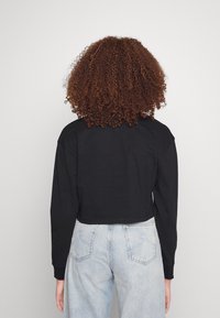 Black cropped long-sleeve shirt with a round neckline, soft texture, and relaxed fit, paired with light blue high-waisted jeans.