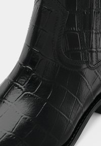 Crne kožne čizme do gležnja s sjajnom teksturom krokodila i ušivenim detaljima, s okruglim vrhom i malim potpeticama.