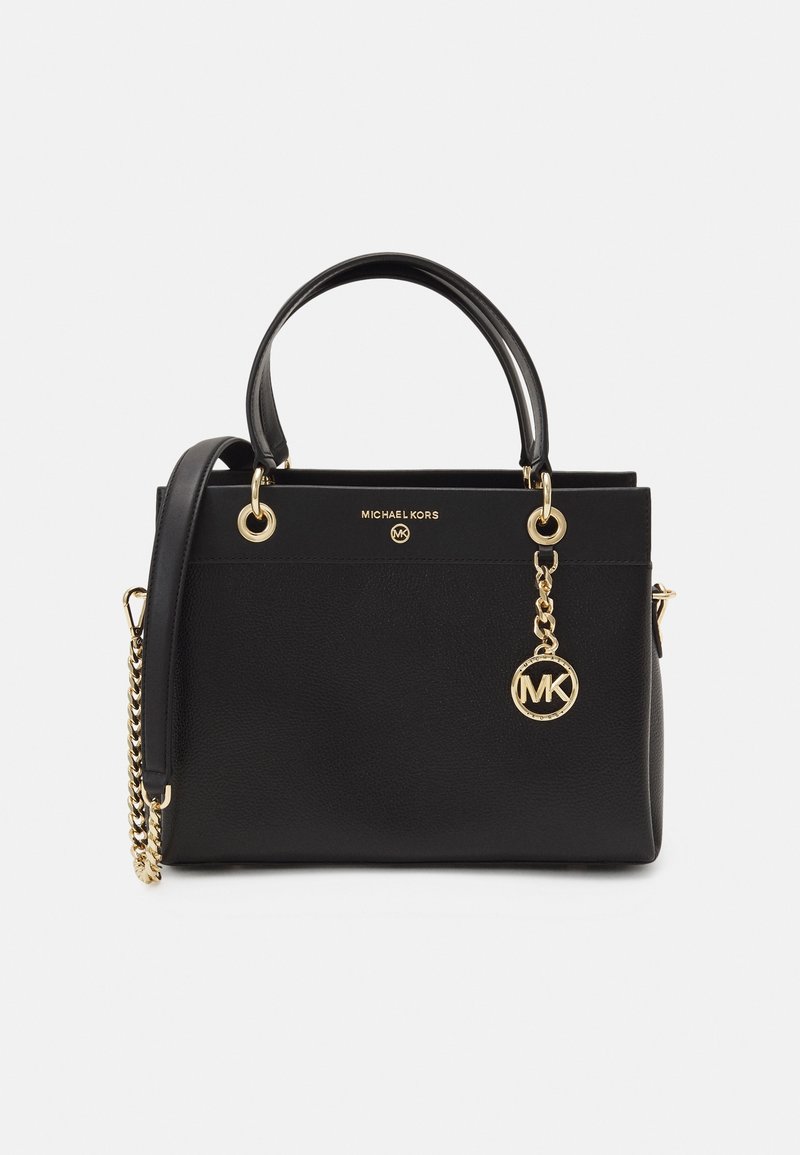 Sac à main en cuir noir à texture granuleuse, avec des poignées supérieures doubles, des accents en métal doré, une anse en chaîne amovible et un pendentif en forme de logo circulaire.