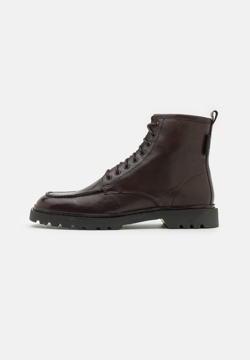 Bottines en cuir marron foncé avec un bout rond, un laçage sur le devant et une semelle texturée. Dotées d'une languette à l'arrière pour un enfilage facile.