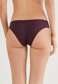 Bordeaux stoffen slips met een gladde, rekbare textuur en een middelhoge pasvorm, voorzien van een naadloze tailleband en minimale dekking aan de achterkant.