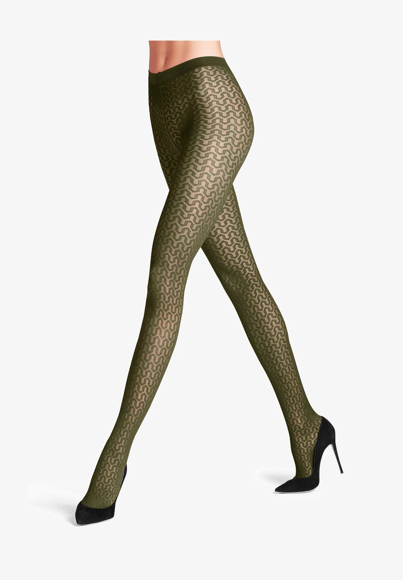 Des collants olive à motif présentent un design en vagues, avec une texture semi-transparente et une taille confortable. Portés avec des talons hauts noirs.