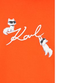 Un tessuto arancione brillante presenta un design di due gatti bianchi che indossano occhiali da sole neri, insieme alla firma "Karl" in testo corsivo bianco.