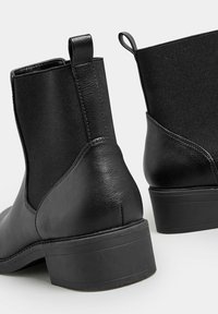 Mustat nilkkurit, joissa on sileä nahkakärki ja pehmeä kangaspaneeli, jossa on vetoketju. Pyöristetty korko ja teksturoitu kumipohja.