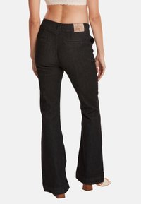 Zwarte flared jeans met een gestructureerde tailleband, voorzien van twee achterzakken, een label op de tailleband en een lichte vervaging aan de zoom.