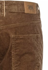 Pantalons en velours côtelé marron avec une surface texturée, une poche arrière et une étiquette en cuir portant la marque "Camel Active" au niveau de la taille.