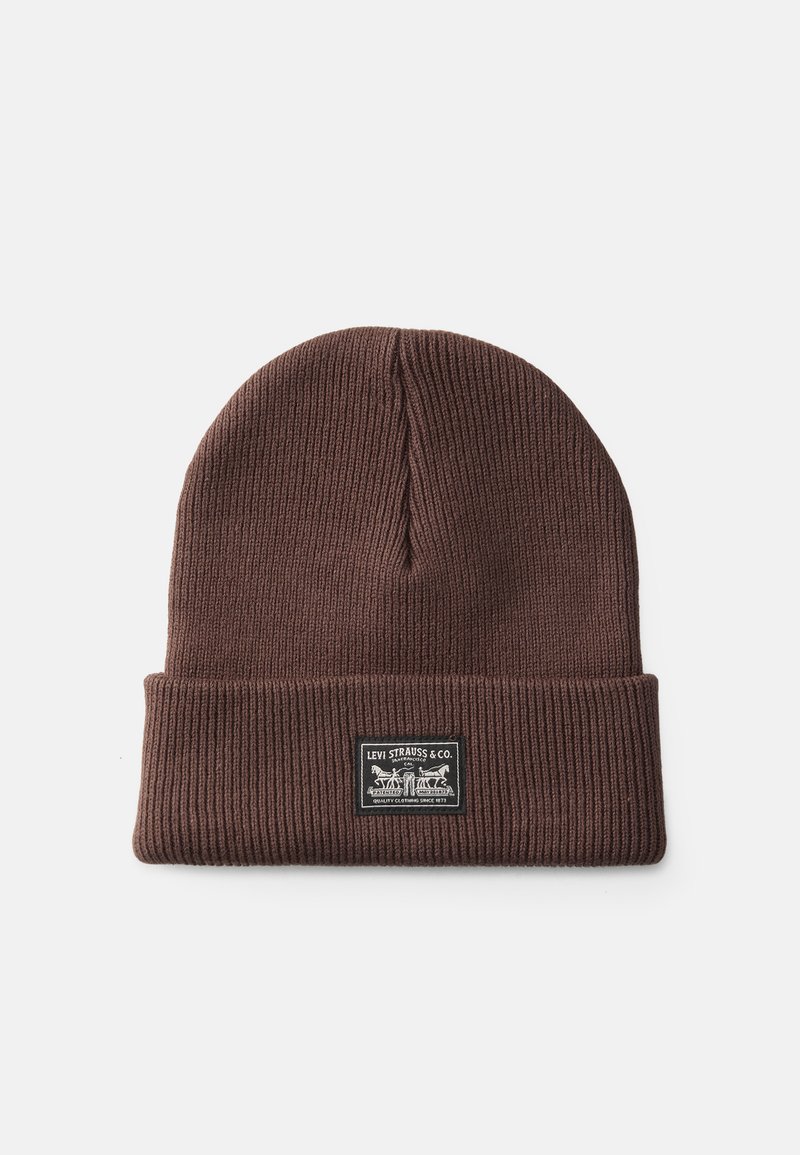Gorro de malha castanho com textura canelada e borda dobrada. Uma etiqueta retangular tecida está costurada na parte da frente com os detalhes da marca.