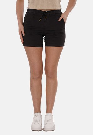 Pantaloni corti neri realizzati in tessuto leggero con vita regolabile, tasche frontali e design aderente. Abbinati a sneakers bianche.