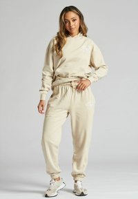 Beżowa bluza z kapturem i dresy wykonane z miękkiego materiału, z przednią kieszenią, elastycznymi mankietami i sznurkiem w talii. Subtelny detal z logo.