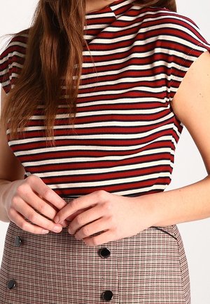 Czerwono-biały, prążkowany top w paski z wysokim kołnierzem i krótkimi rękawkami, zestawiony z kraciastą spódnicą ozdobioną czarnymi guzikami.