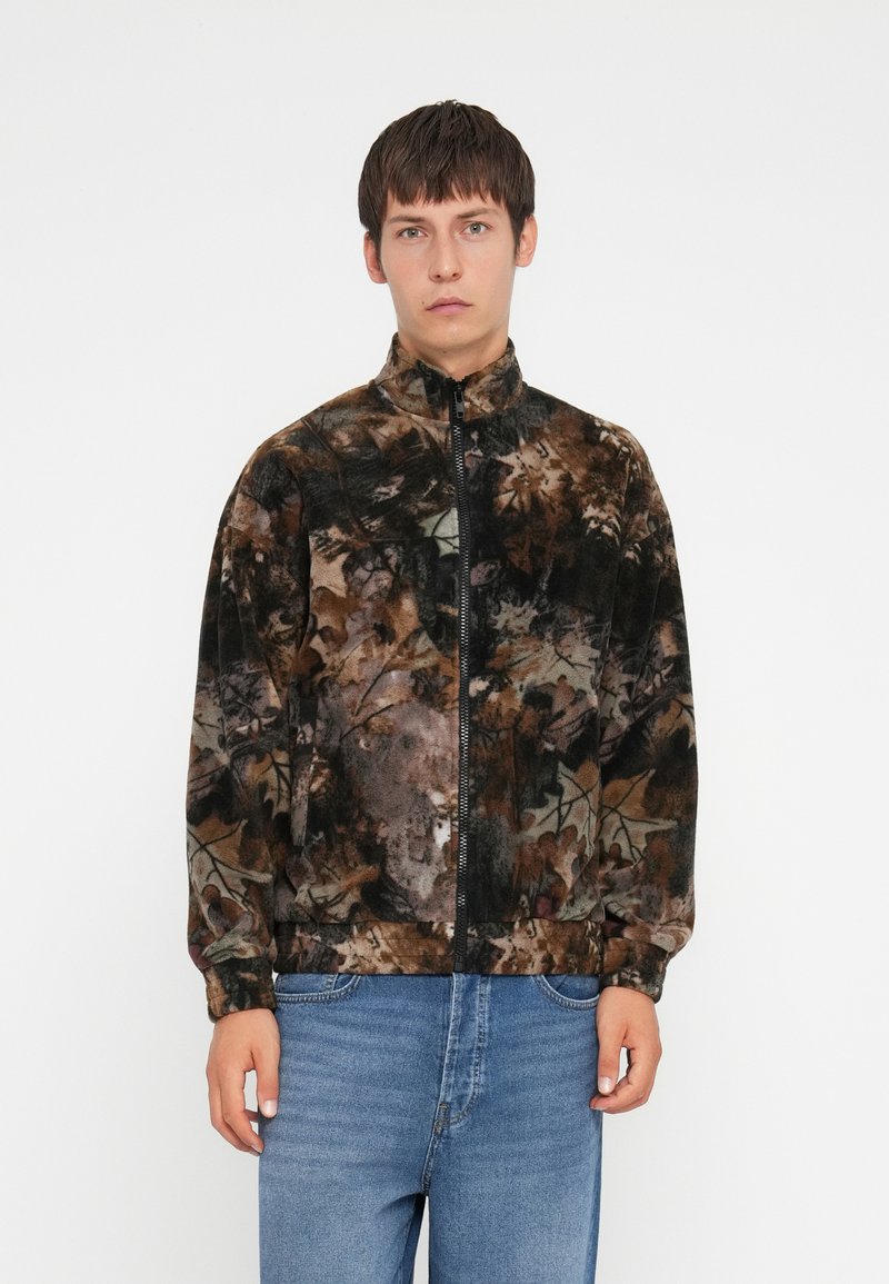 Jachetă din fleece cu guler înalt, având un model de camuflaj multicolor în nuanțe de maro, verde și negru. Închidere cu fermoar, man�șete elastice.