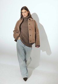 Bruine suède jacket over een bruine coltrui, gecombineerd met lichtblauwe wijde jeans en donkere pumps met spitse neuzen.