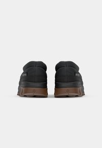 Svart puffer-sneakers med en teksturert overdel og brune gummisåler, med et karakteristisk mønster for grep og forsterkningselementer.