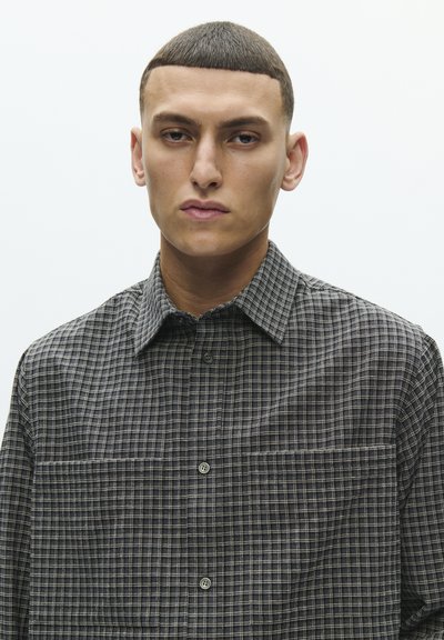 Košulja na kopčanje s uzorkom crnih i sivih kariranih kvadrata, sa širokim ovratnikom i džepom na prsima, izrađena od teksturiranog tkanja.