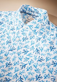Lyhythihainen valkoinen paita, jossa sininen korallikuvio. Napit edessä ja klassinen kaulussuunnittelu. Pehmeä rakenne.