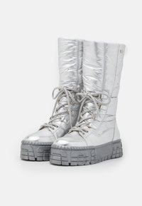 Botas metálicas plateadas hasta la rodilla con parte superior acolchada, puntera redonda y suela gris gruesa; cuentan con cordones y patrones texturizados.