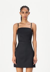 Robe mini noire ajustée avec des fines bretelles, décolleté carré et texture lisse. Présentant un petit logo près de la taille.