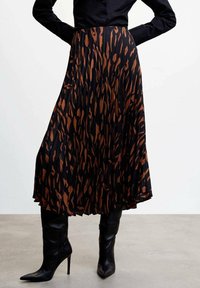 Falda negra con pliegues y un patrón de estampado animal en tonos marrones, combinada con botas negras de tacón altas hasta la rodilla, exhibiendo una silueta fluida.