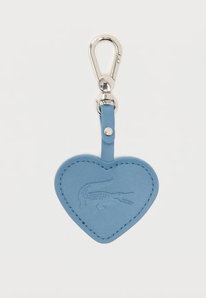 Llavero de cuero azul claro en forma de corazón con logo de cocodrilo en relieve y cierre de metal plateado sobre fondo blanco.