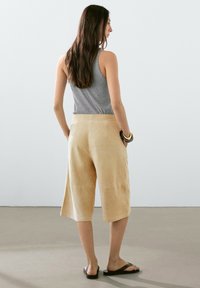 Tan suède culottes met een elastische tailleband, midi-lengte en een gladde textuur. Gekleed met een grijze mouwloze top en zwarte sandalen.
