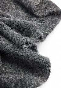 Tela de lana gris colgada, con una textura suave y peluda, fibras visibles y pliegues suaves, que crean una apariencia acogedora.