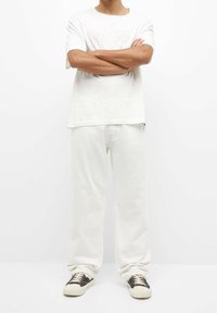 White short-sleeve t-shirt with a rounded neckline, paired with loose-fitting white jeans and black sneakers with white soles.