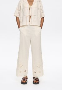 Beige geborduurde crop top met korte mouwen, gecombineerd met crèmekleurige broek met wijde pijpen en ingewikkelde bloemenpatronen in een relaxed fit.