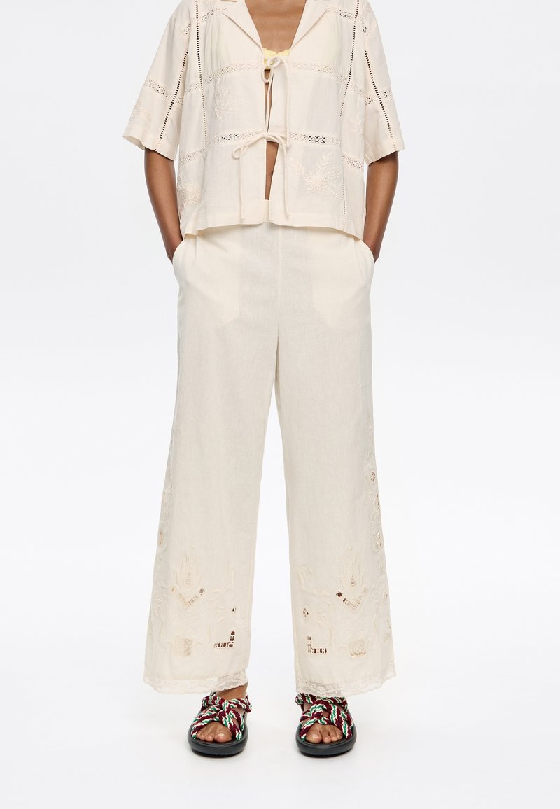 Beige geborduurde crop top met korte mouwen, gecombineerd met crèmekleurige broek met wijde pijpen en ingewikkelde bloemenpatronen in een relaxed fit.