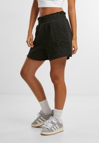 Svart sweatshorts med elastisk midje, sidelommer, slitt hem og brodert sommerfugl-detalj på benet. Kombinert med grå sneakers.