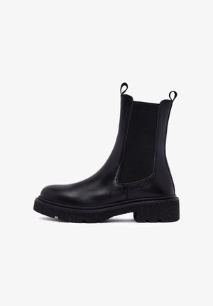 Botín de cuero negro hasta el tobillo con paneles laterales elásticos y una suela texturizada y gruesa. Presenta tiradores en los laterales para facilitar su colocación.