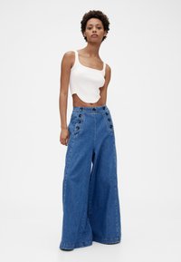 Högmidjade vida jeansbyxor i ljusblått med stora svarta knappar framtill och rå kant nedtill. Matchas med en croppad vit topp.