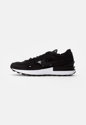 Basket basse noire avec dessus en mesh et daim, semelle intermédiaire blanche, semelle extérieure noire et détail superposé au talon.
