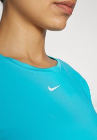 T-shirt de sport bleu clair en matériau lisse et extensible, avec un col rond et un petit logo Nike blanc sur la poitrine.