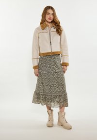 Lys beige cropped jakke med brun fake pelskrave og manchetter, båret over en floral-printet lagdelt kjole og beige snørebåndsstøvler.