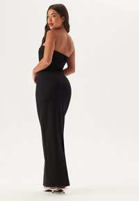 Jumpsuit nero senza spalline con strisce verticali bianche, design aderente e texture liscia. Presenta una gamba ampia e hardware minimale.
