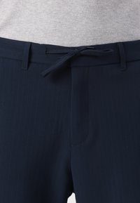 Marineblaue Nadelstreifenhose mit flachem Bund, passendem Kordelzug und Seitentaschen, aus glattem Stoff gefertigt.
