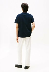 Camisa de manga corta azul marino con cuello redondo, combinada con pantalones blancos y zapatos negros; textura suave, diseño sencillo y corte relajado.