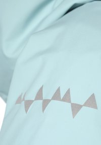 Lysblå stof med en tekstureret overflade og et mønster af uregelmæssige, trekantede former i en metallisk grå nuance langs kanten.