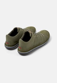 Olive green shoes with a textured canvas upper, elastic laces, and a rubber sole featuring a contrasting blue stripe and red logo accent.