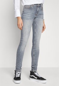Vaqueros de mezclilla azul claro, delgados, con detalles de desgaste, costuras claras, diseño de cinco bolsillos, usados con zapatillas negras de caña alta.