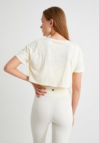 Beskåret, lysegul t-shirt med en tekstureret finish. Har korte ærmer og en rund halsudskæring. Kombineret med højtaljede hvide leggings.