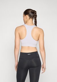 Hellgraues sportliches Crop-Top mit Racerback-Design, kombiniert mit schwarzen hoch sitzenden Leggings. Nahtlose Textur und minimale Markenkennzeichnung.