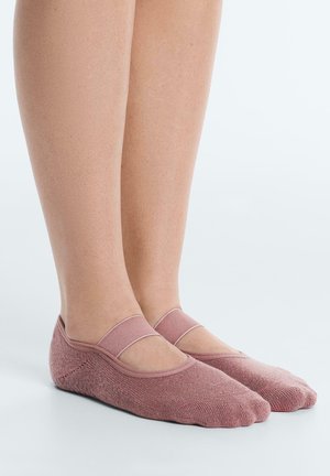 Lábak, halvány rózsaszín csúszásgátló zokniban, amelyek rugalmas pántokkal rendelkeznek, világos, sima felületen állnak.