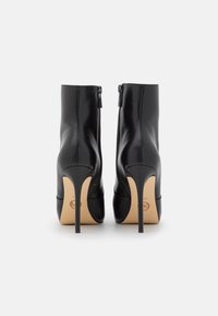 Stivaletti neri in pelle con tacchi a stiletto alti, chiusura con cerniera e una texture liscia. Le suole sono beige con un logo brandizzato.