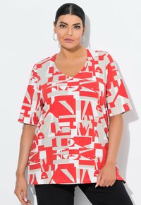 Červené a béžové grafické tri čko s výstřihem do V a krátkými rukávy, zdobené abstraktními tvary a textovými vzory, vyrobené z lehkého materiálu.