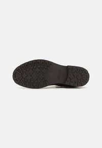 Semelle en caoutchouc noir avec un motif de grip texturé, présentant des rainures profondes et des accents surélevés pour une meilleure adhérence. Construction robuste et durable.
