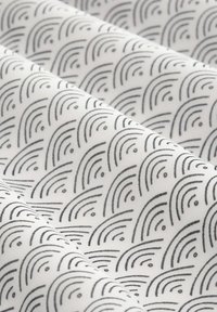 Tessuto di cotone con motivi ad arco neri ripetuti su sfondo bianco con piccoli accenti circolari, dalla texture leggermente rugosa e morbida.