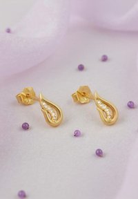 Orecchini a goccia in oro con una fila di piccole pietre trasparenti lungo un bordo, circondati da perline viola su uno sfondo morbido.
