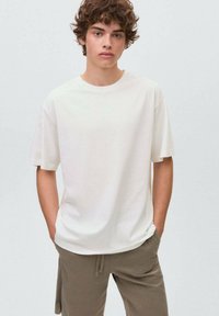 Bílý bavlněný tričko s kulatým výstřihem, krátkými rukávy a volným střihem, kombinované s olivovými kalhotami na šňůrku.